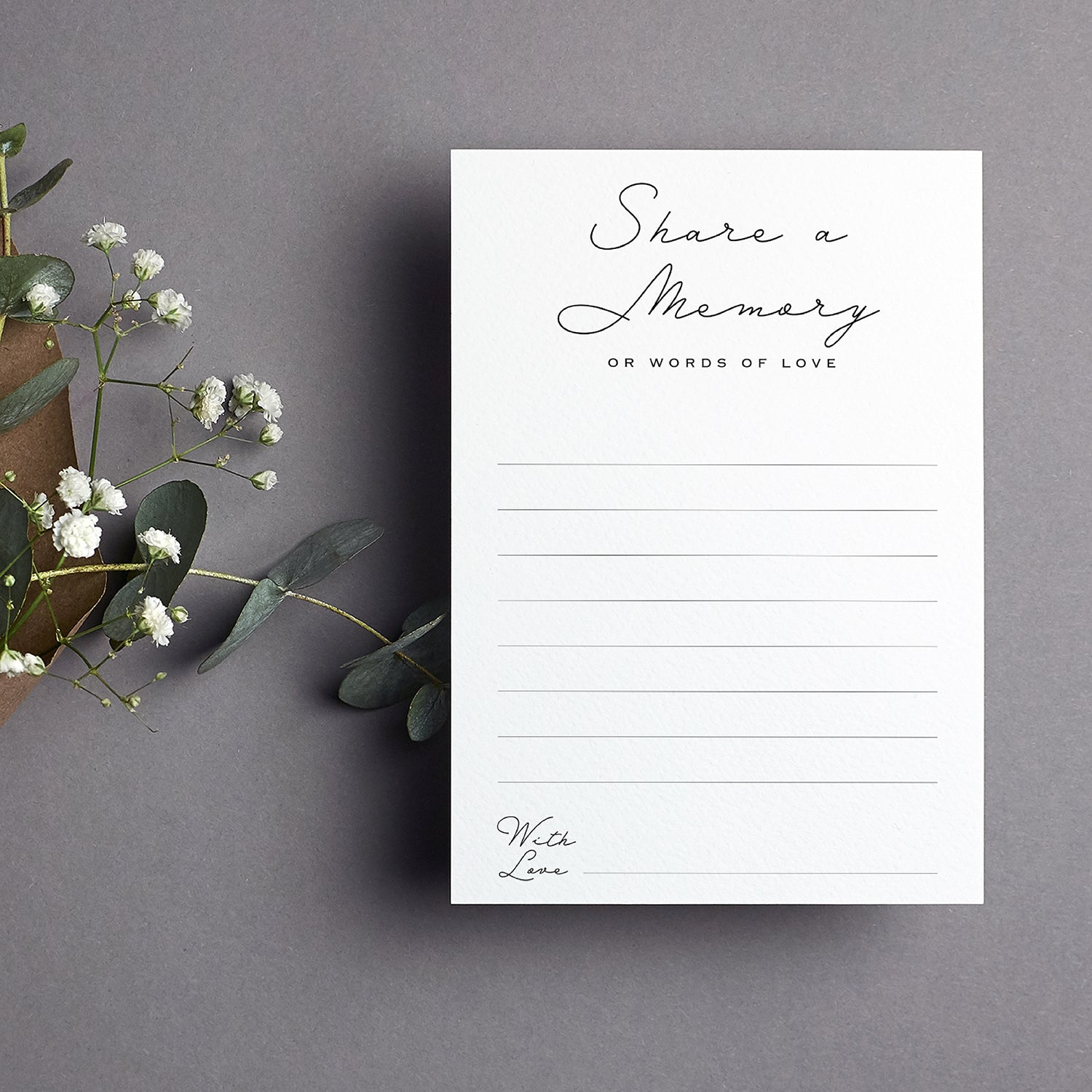 cardamonoly share a memory cards on grey desk with olive foliage, small white flowers and kraft envelope