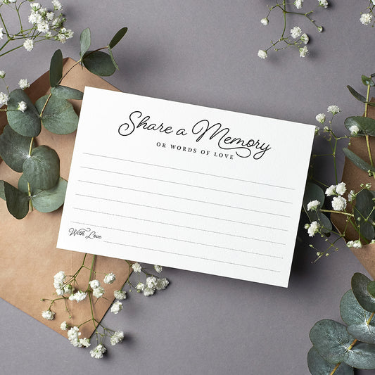 cardamonoly share a memory cards on grey desk with olive foliage, small white flowers and kraft envelope